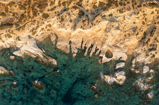 Aerial view of rugged cliffs meet the turquoise sea, the sun casting long shadows on the white rocks, creating a dramatic coastal scene, Fira, Thira, Greece.