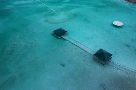 Aerial view of a weathered pier stretching into the tranquil turquoise waters, contrasting with the stark white of a solitary parasol, Arad, South District, Israel.