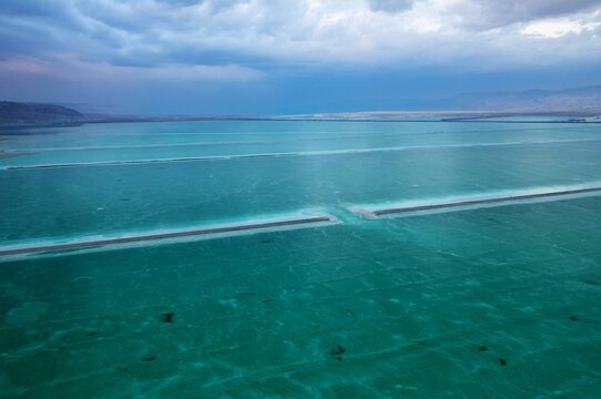 Aerial view of the mesmerizing turquoise waters of the Dead Sea shimmer under a moody sky, contrasting with the stark, mineral-rich shores, Arad, South District, Israel.