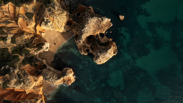 Aerial view of golden cliffs meet the teal ocean, where hidden beaches nestle in the embrace of rugged rock formations, Lagos, Faro District, Portugal.