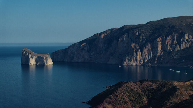 Aerial view of the imposing Pan di Zucchero rock formation stands sentinel amidst the tranquil blue waters, Masua, Sardegna, Italy.