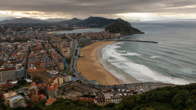 Aerial view of the golden sands of La Concha Beach meet the turbulent Atlantic waters beneath a brooding sky, with Monte Urgull standing guard, Donostia, Basque Country, Spain.
