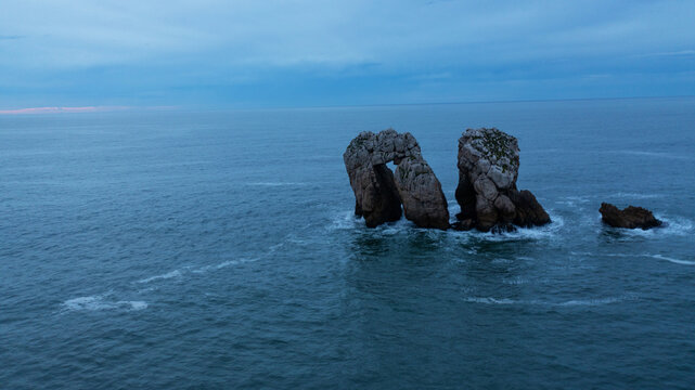 Aerial view of the dramatic rock formations piercing through the still, dark waters of the Bay of Biscay, a serene yet powerful scene, Donostia San Sebastian, Basque Country, Spain.