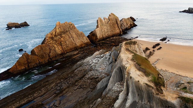 Aerial view of rugged cliffs meet the tranquil beach, where golden sands contrast with the deep blue sea, Donostia San Sebastian, Basque Country, Spain.