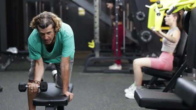 Adult man does back exercises with dumbbells in the gym, he works hard to develop muscle strength and build an athletic figure. High quality 4k footage