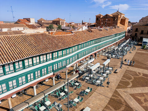 Aerial view of the Plaza Mayor with its iconic green colonnades casting shadows on the patterned pavement, a vibrant hub of activity under the Spanish sun, Almagro, Castile-La Mancha, Spain.