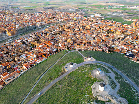 Aerial view of windmills standing guard over the town, their white forms contrasting with the green hill and the warm terracotta rooftops, Consuegra, Castile-La Mancha, Spain.