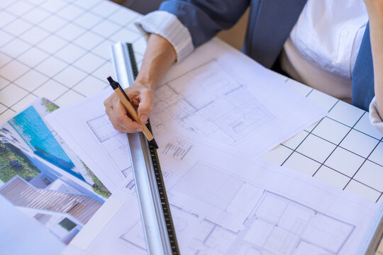 Architect drawing with ruler and blueprints at a planning workspace