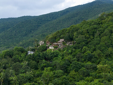 Aerial view of verdant mountain slopes blanketed in dense tropical foliage, dotted with rustic dwellings at Bukit Love, Karimunjawa, Jawa Tengah, Indonesia.