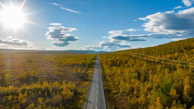 Aerial view of a seemingly endless road cuts through a tapestry of autumnal hues, under a vast sky in Enontekio Kilpisjarvi, Lappi, Finland.