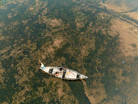 Aerial view of a solitary boat adrift in a murky river, its weathered hull contrasting with the algae-covered water, Rajbari, Bangladesh.
