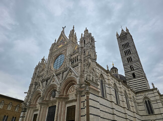 Obraz premium Facade and Bell Tower of Siena Cathedral (Duomo di Siena), Italy. Ornate Gothic Architecture with Marble Stripes and Rose Window under Cloudy Sky in Tuscany. Historic Italian Landmark