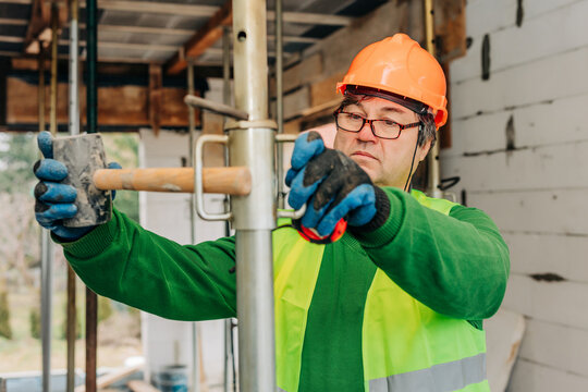 Worker in hard hat and vest measuring at construction site indoors