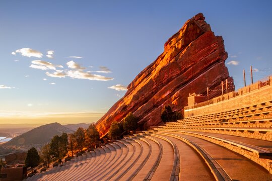 View of the iconic Red Rocks Amphitheatre glows warmly in the morning light, contrasting with the cool blues of the distant mountains, Morrison, Colorado, United States.