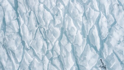 Fototapeta premium Top view of broken ice floes and deep cracks on a frozen lake. Detailed winter background with cold blue textures.