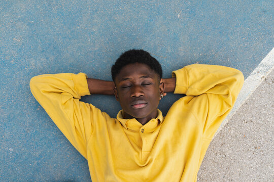 Young black man sleeping on floor, with hands behind head
