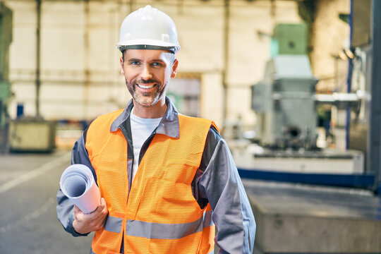 Portrait of smiling man holding blueprints in factory