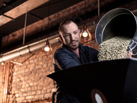 Mann pouring green coffee beans in coffee roaster