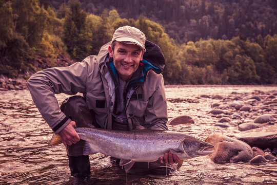 Fly fisherman smiling while holding caught salmon fish in river