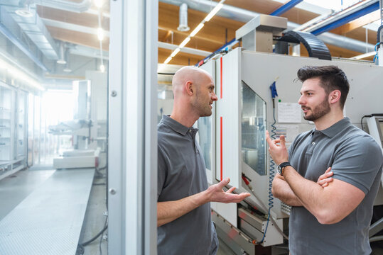 Two men discussing at machine in modern factory