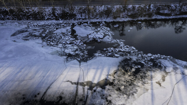 Aerial view of the Schuylkill River partially frozen, reflecting stark winter light, with ice floes creating a mosaic of white and blue textures, Philadelphia, Pennsylvania, United States.