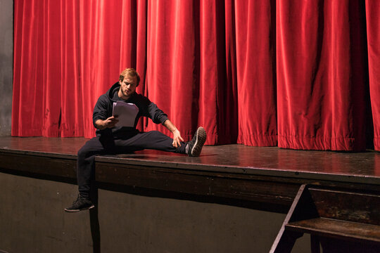 Actor sitting on stage of theatre studying script