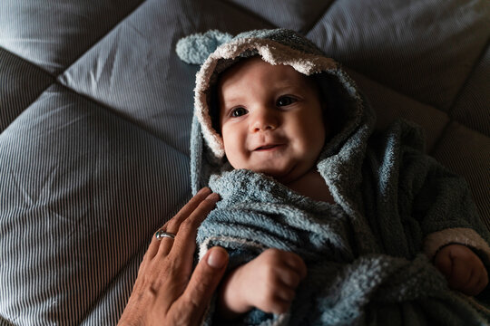 Portrait of baby girl lying on bed wrapped with shark shaped towel touched by mother's hand