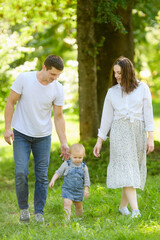 Fototapeta premium Family walk outdoors, parents walking alongside toddler, keeping them safe. Walk outdoors, where adults support and guide toddler. Family vacation concepts