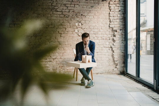 Businessman sitting at brick wall looking at architectural model