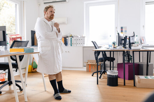 Businessman wearing bathrobe in office holding cup