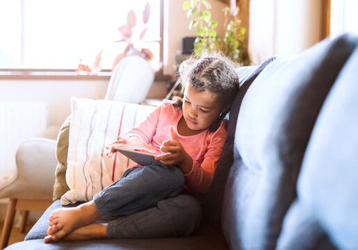 Little girl using sitting tablet, sitting on couch