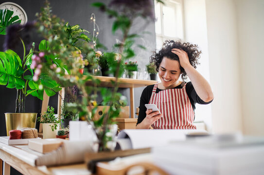 Happy young woman using cell phone in a small shop with plants