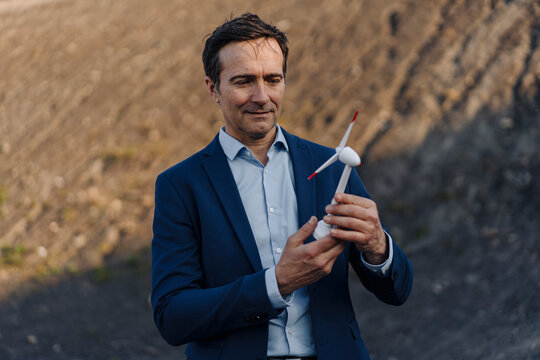 Mature businessman on a disused mine tip holding wind turbine model