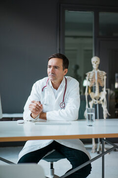 Doctor sitting at desk in medical practice with skeleton in background