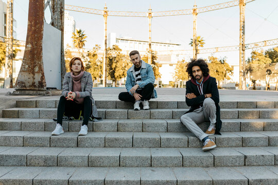 Portrait of three serious friends sitting on stairs
