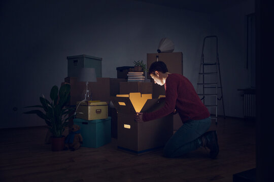 Woman looking into shining cardboard box in a new home