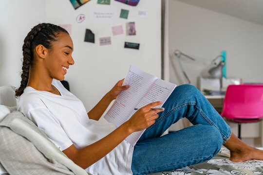 Teenage girl reading in exercise book sitting on bed at home