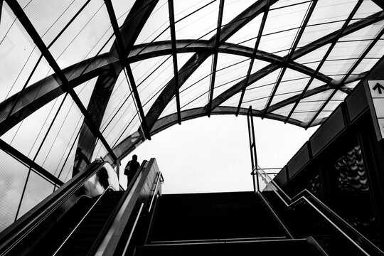 A monochrome station escalator in an urban transit interior where glass structure lines and symmetry lead to a silhouette within modern architecture