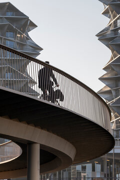 A pedestrian silhouette on a modern Copenhagen bridge with a curved walkway and sleek architecture where urban railing lines frame a contemporary crossing