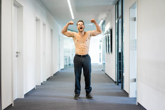 Screaming barechested businessman flexing muscles in office
