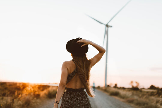 Back view of young woman on rural road in the evening with wind wheel in the background