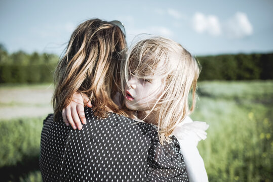 Portrait of little girl on her mother's arms in rape field
