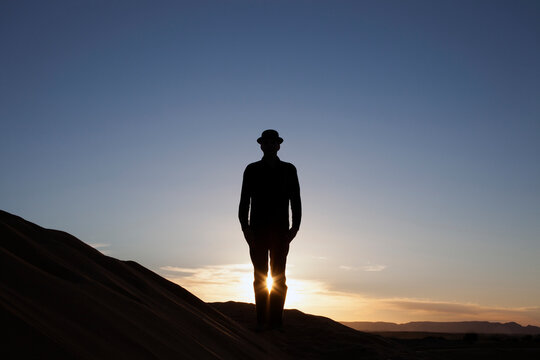 Morocco, Merzouga, Erg Chebbi, silhouette of man wearing a bowler hat standing on desert dune at sunset