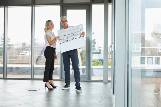 Businessman and woman standing in office, discussing blueprint
