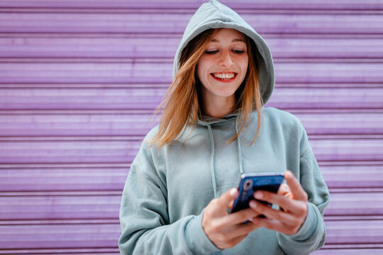 Portrait of young blonde woman with green hoodie and purple background