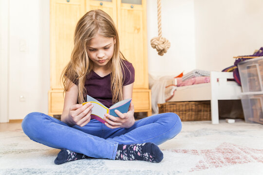 Girl sitting on the floor of children's room reading a book