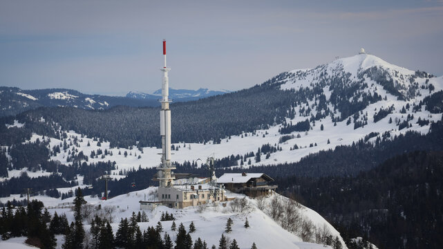 Aerial view of Petit Mont Rond and Col de la Faucille, a tall radio tower, and a cozy building nestled against the snowy landscape, Echenevex, Auvergne-Rhone-Alpes, France.