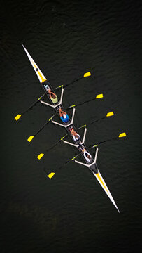 Aerial view of a sleek rowing shell slicing through the dark, reflective waters, each stroke a burst of bright yellow against the deep backdrop, Divonne-les-Bains, Auvergne-Rhone-Alpes, France.