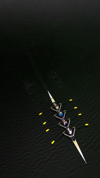 Aerial view of a sleek rowing boat slicing through the dark, reflective waters, its oars creating golden splashes, Divonne-les-Bains, Auvergne-Rhone-Alpes, France.