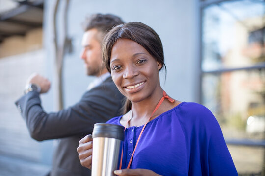 Portrait of smiling businesswoman with coffee mug and businessman in background